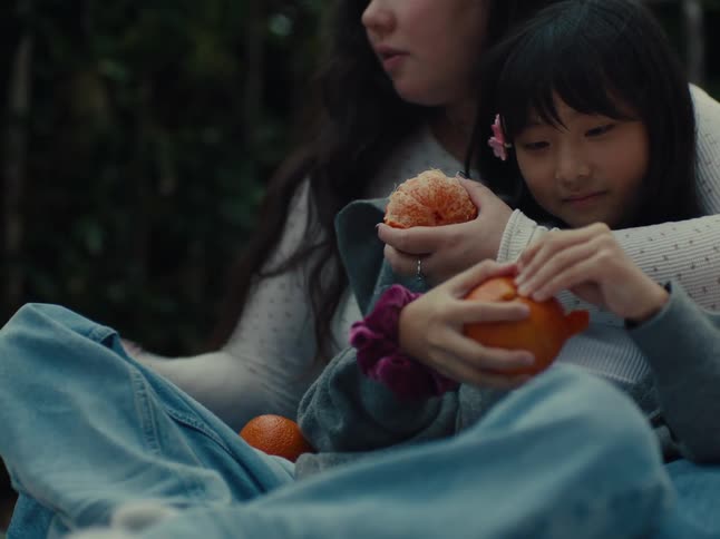 Two girls one with a pink flower in her hair peel oranges outdoors