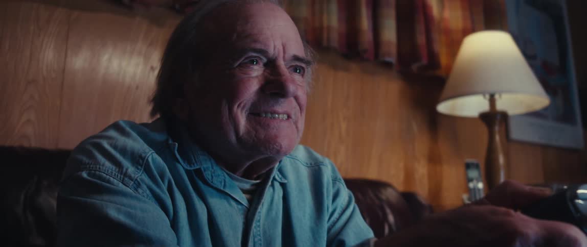 An elderly man with an intense and excited expression grinning broadly as he plays a video game holding a controller in his hands and winning the game