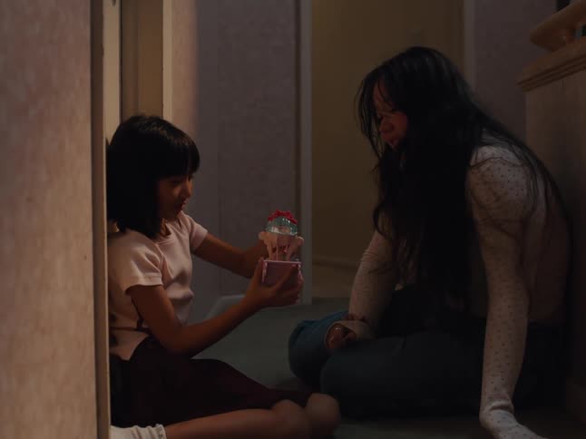 A young girl and a woman with long dark hair sit on the floor and the girl plays with a small toy