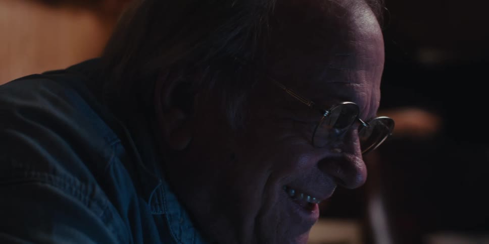 A happy elderly man is sitting on a couch at home using a laptop