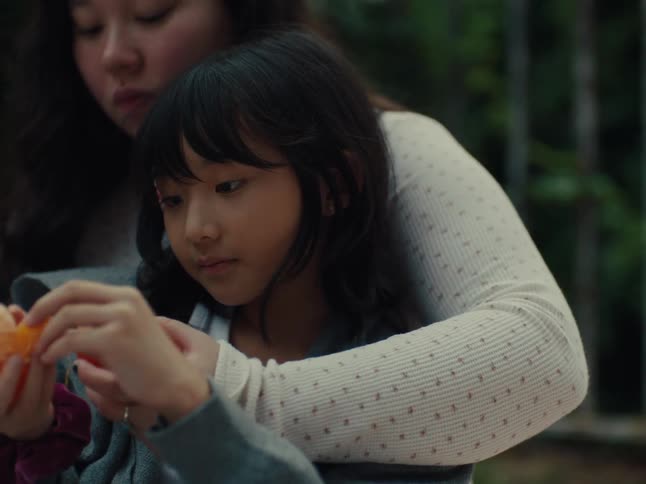 Little girl sitting with her arms around a teenage girl as they both eat an orange