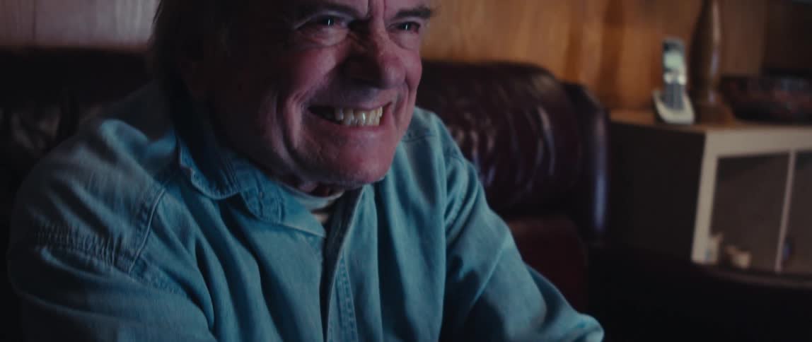 An older man with an intense and excited expression grinning broadly as he plays a video game holding a controller in his hands