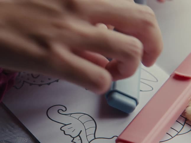 A childs hand shaking a blue object on top of a paper with drawings of animals and then an adult hand starts to do the same
