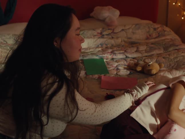 Older sister cuddling younger sister who is lying on the bed holding a teddy bear