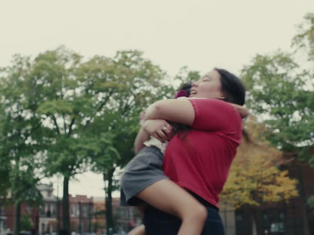 Little girl jumping on her older sisters lap and hugging while they are outdoors