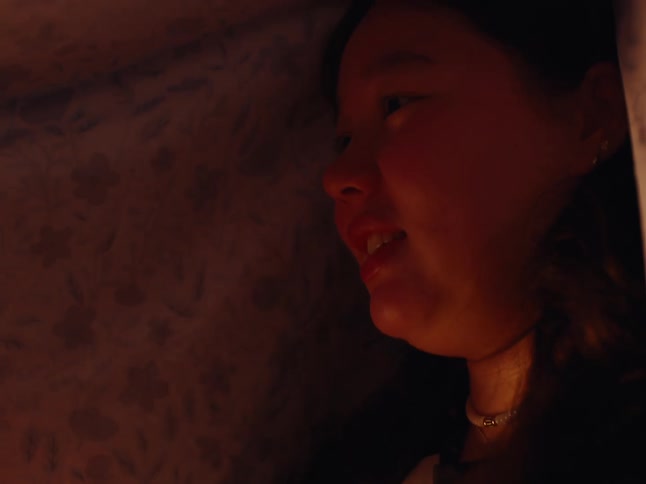 A mother and daughter play rock paper scissors under a blanket at night