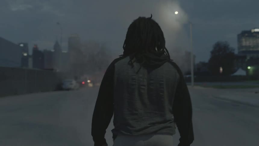 A man walking in a parking lot area watching a car and lights flashing with some smoke from somewhere