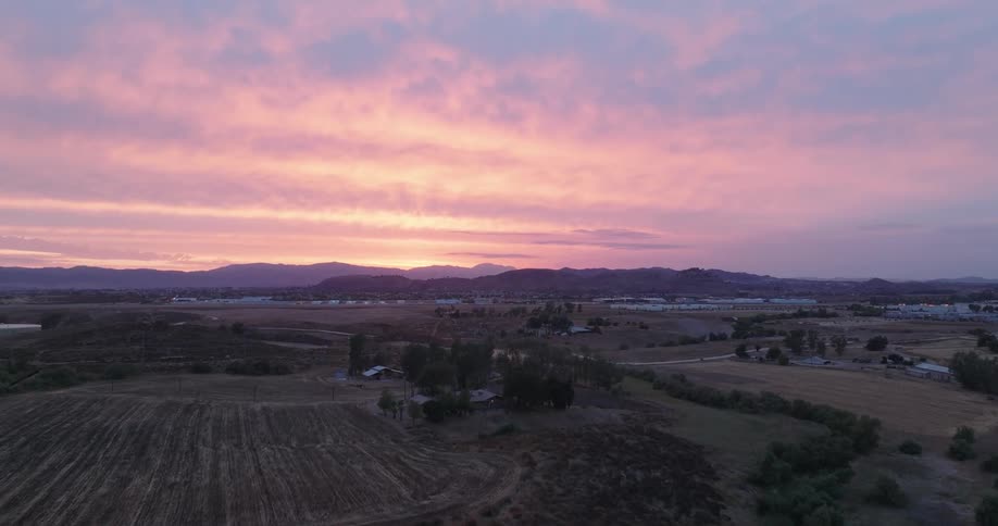 A sunset casts a soft pink hue over a rolling landscape dotted with farms and distant mountains