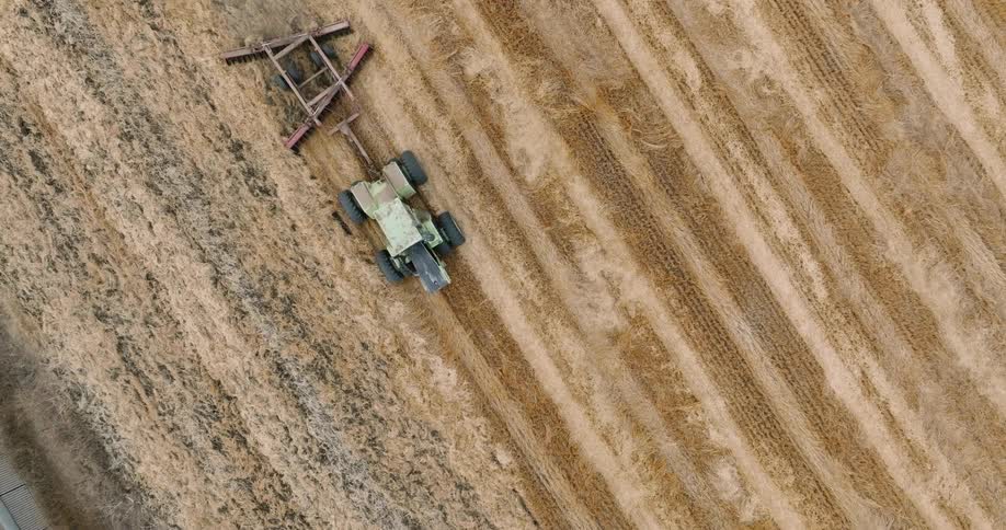 An aerial view of a tractor plowing a field creating parallel lines in the soil
