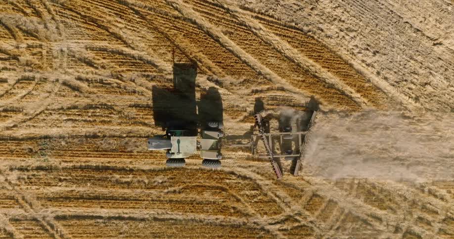 A tractor carves curved lines into a vast parched field as it prepares the soil for planting