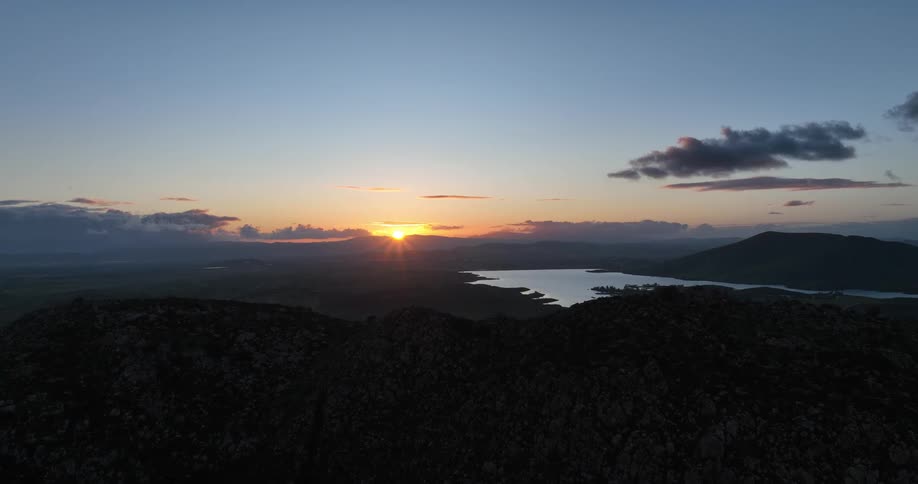 The sun sets behind a jagged mountain range casting a warm glow on the clouds above