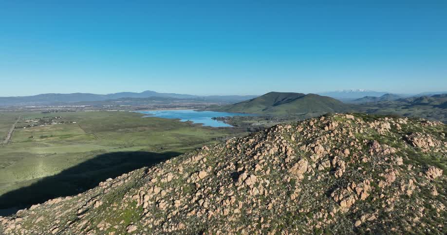 A rugged mountain landscape with a shimmering lake nestled in the valley below and snowcapped peaks in the distance all under a vibrant blue sky