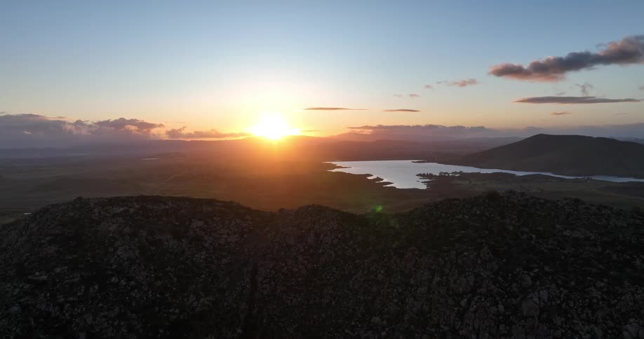 The sun rises over the mountaintop casting hues of orange and pink across a vast rugged landscape dotted with lakes