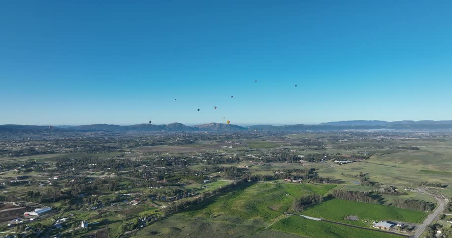 Aerial view of residential neighborhoods located in green areas with flying balloons and mountain ranges in the background