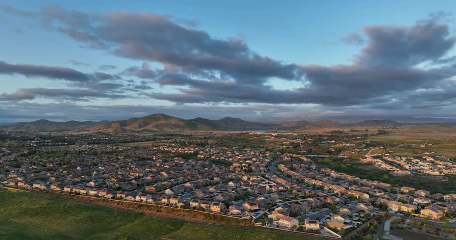 A sprawling suburban landscape stretches towards distant mountains under a dramatic twilight sky