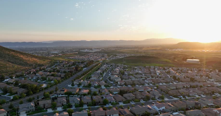 A picturesque suburban landscape bathed in the golden hues of sunset with a winding road snaking through a sprawling neighborhood nestled amidst rolling hills