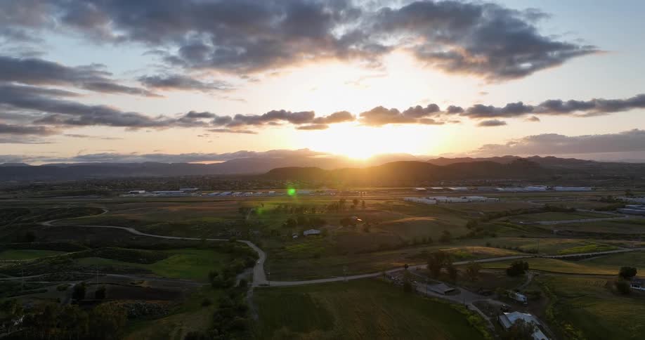 A golden sunset illuminates a rolling landscape dotted with farms and distant mountains