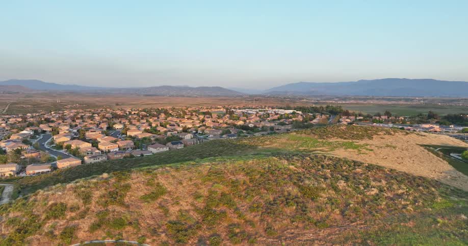 A sprawling suburban neighborhood nestled in a valley with rolling hills and a distant mountain range in the background