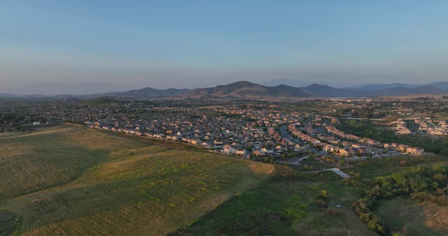 Aerial view of a vast residential area nestled between rolling hills with a clear blue sky overhead