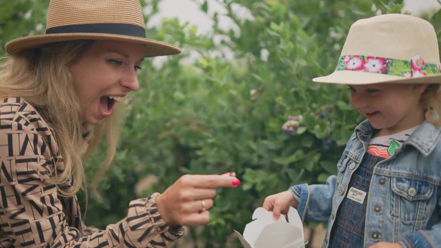 Mother holding an insect next to her young daughter in an outdoor setting with trees around