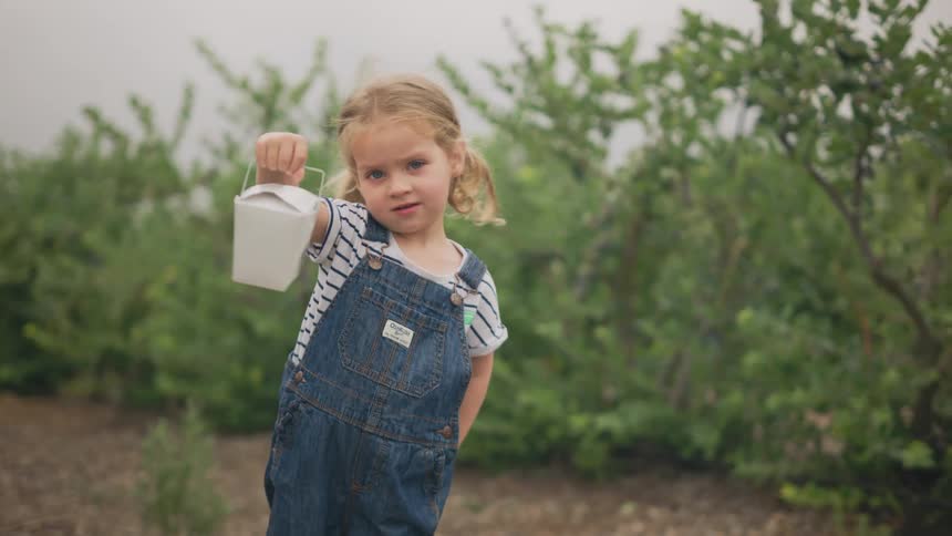 Little girl outdoors with trees around holding two white boxes