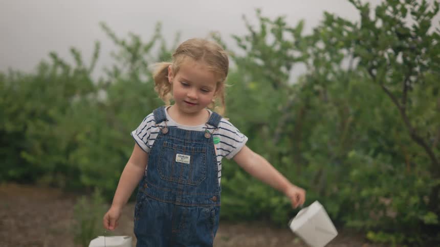 Little blonde girl in a treelined environment holding two small white boxes