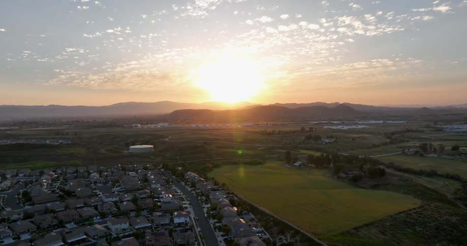 The sun dips below the horizon casting a golden glow over the rolling hills and suburban landscape