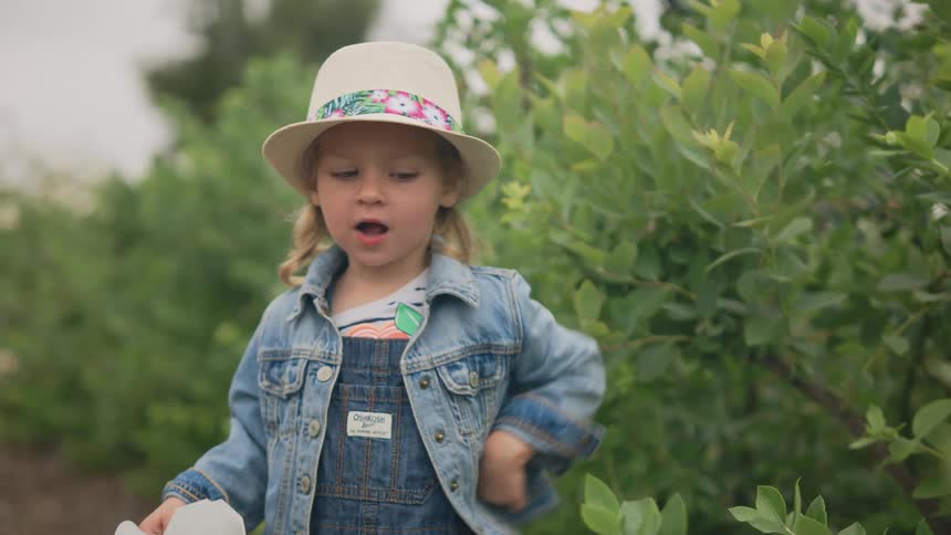 Little blonde girl eating fruit in an outdoor setting with trees in the background