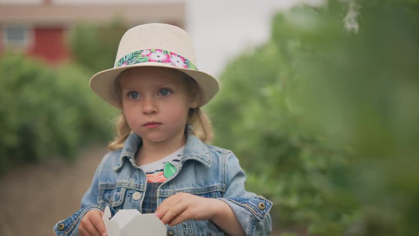 A little blonde girl in a denim jacket and a white hat looking forward