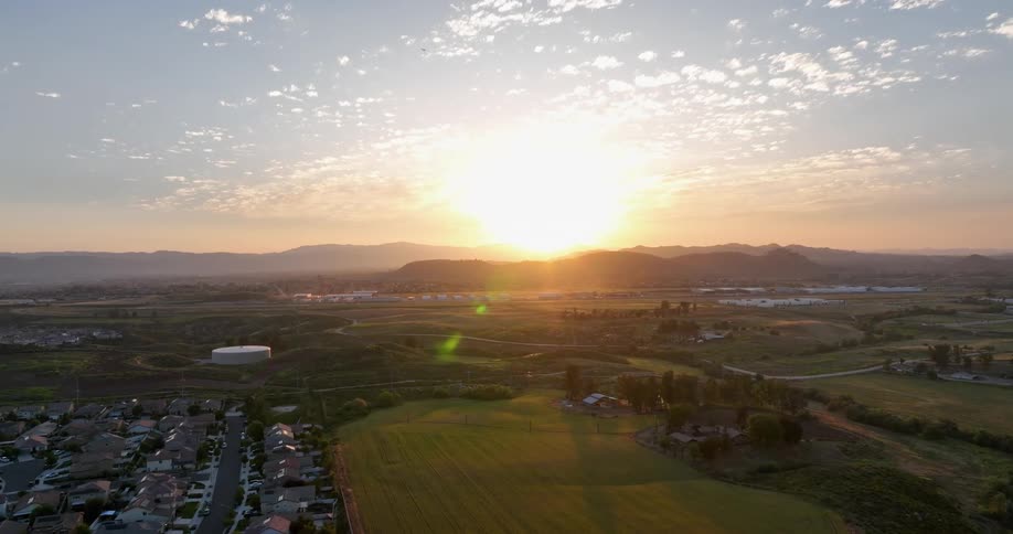 Aerial view of a residential neighborhood next to green areas and sunrise on the horizon