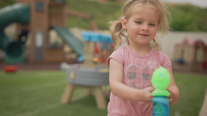 A little girl with pigtails plays with a bubble gun in a backyard