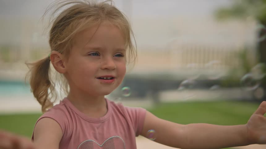Blonde girl smiles while playing with floating bubbles outdoors