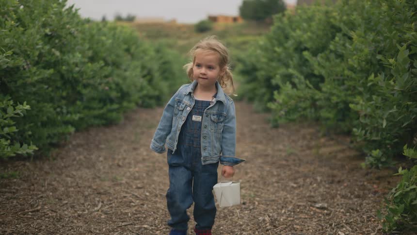 A girl with blonde hair walking down a path surrounded by bushes