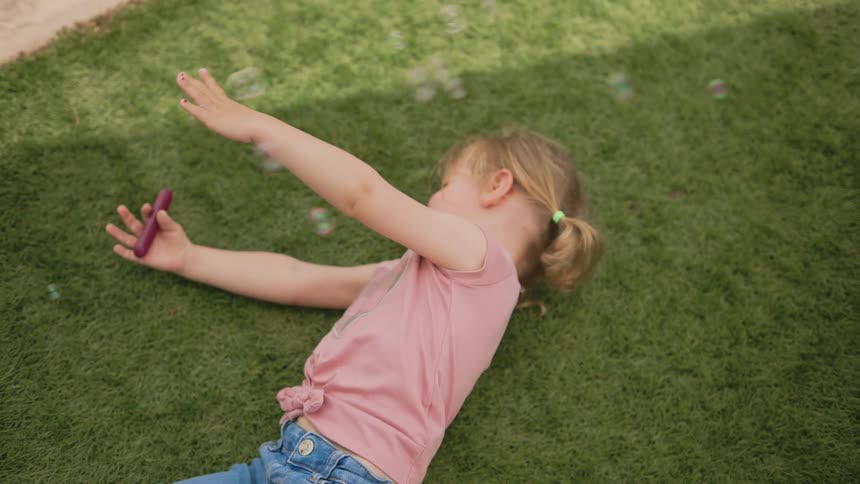 Little girl lying on the grass and soap bubbles flying