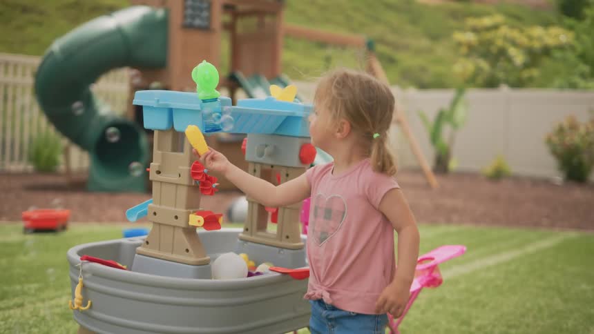 A girl with pigtails is playing with bubbles on a play area in the backyard