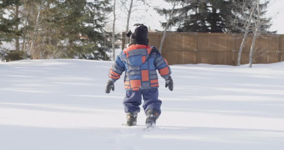 A young boy walks across a snowy yard