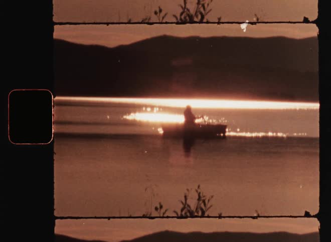 Person rowing a canoe or small boat on a lake at sunset in the mountains while the sun shines into the reflecting surface of the body of water
