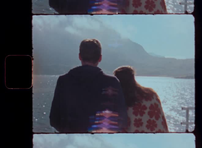 Two people on a boat traveling across a body of water with mountains in the background and soft sunlight creating a warm nostalgic atmosphere as they face each other in conversation
