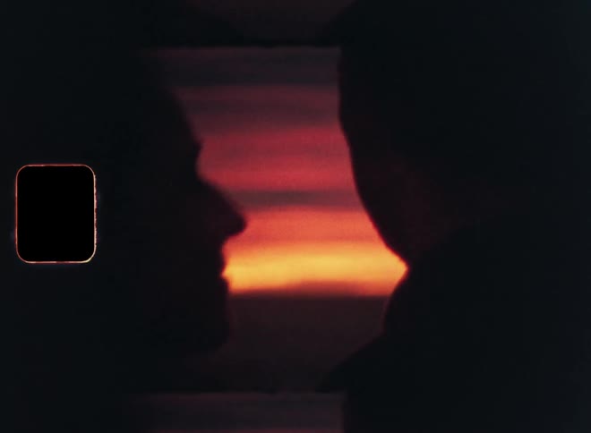 Woman kisses man on the cheek while they watch the sunset