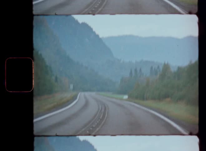 A winding road cuts through a misty landscape with mountains in the distance