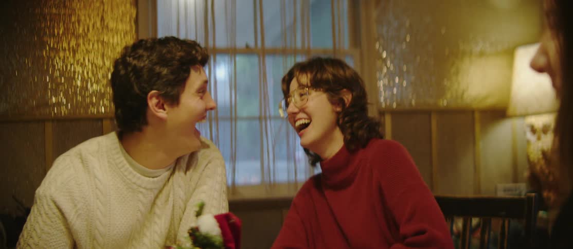 A man and a woman are sitting in a room that is lit by yellow light and they are laughing while talking