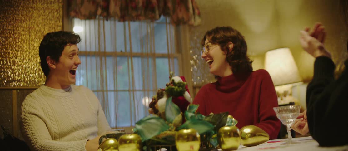 Friends sitting at a table decorated with a centerpiece of green leaves and golden ornaments engaging in conversation and drinking