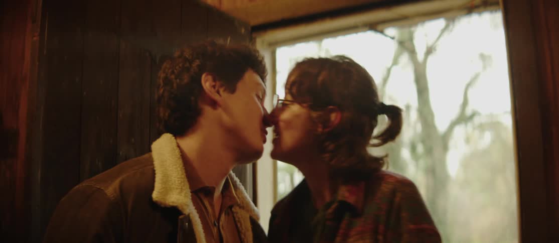 A man and a woman enter a cabin sharing a brief kiss