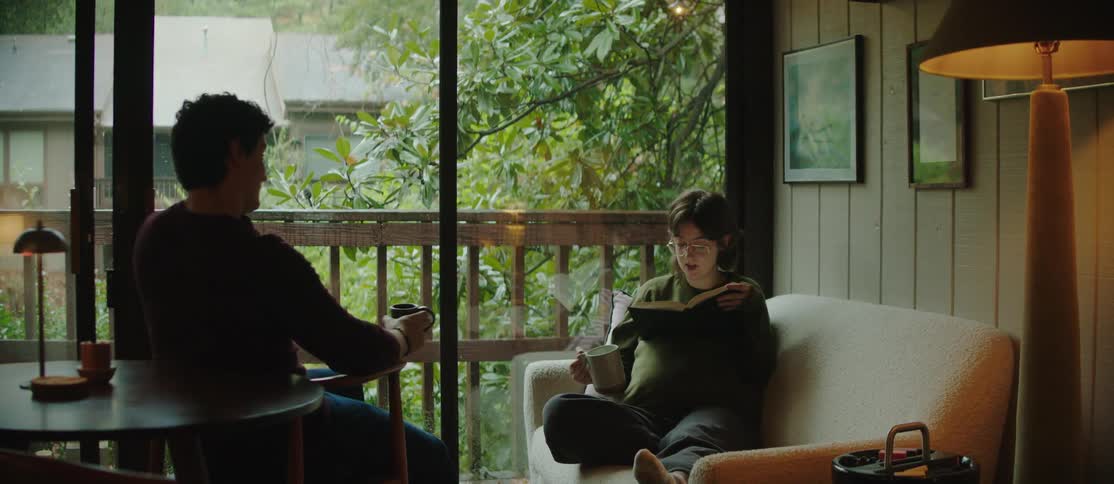 Couple in a living room with a woman reading a book and holding a mug