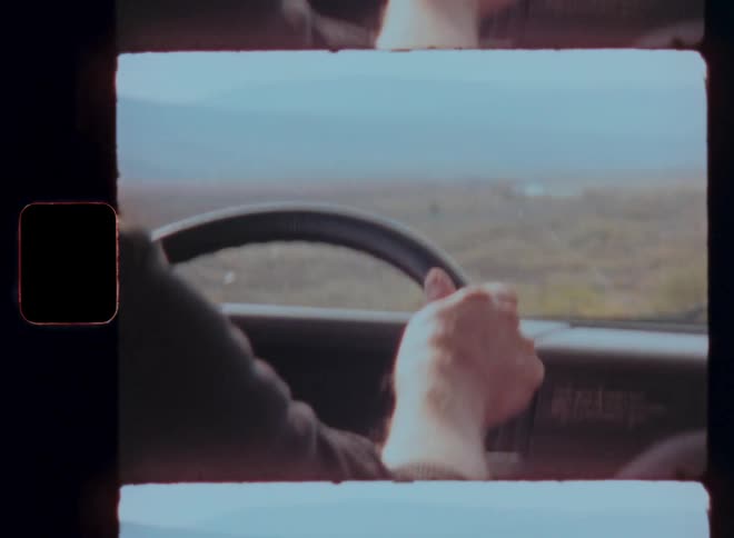 A person is driving a vehicle with one hand on the steering wheel