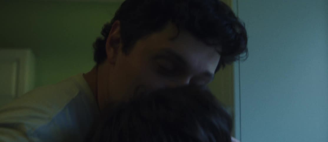 Man kissing his girlfriend who is looking out the window in the kitchen