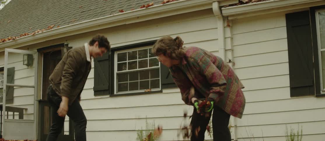 Man and woman picking up leaves and playfully tossing them at each other