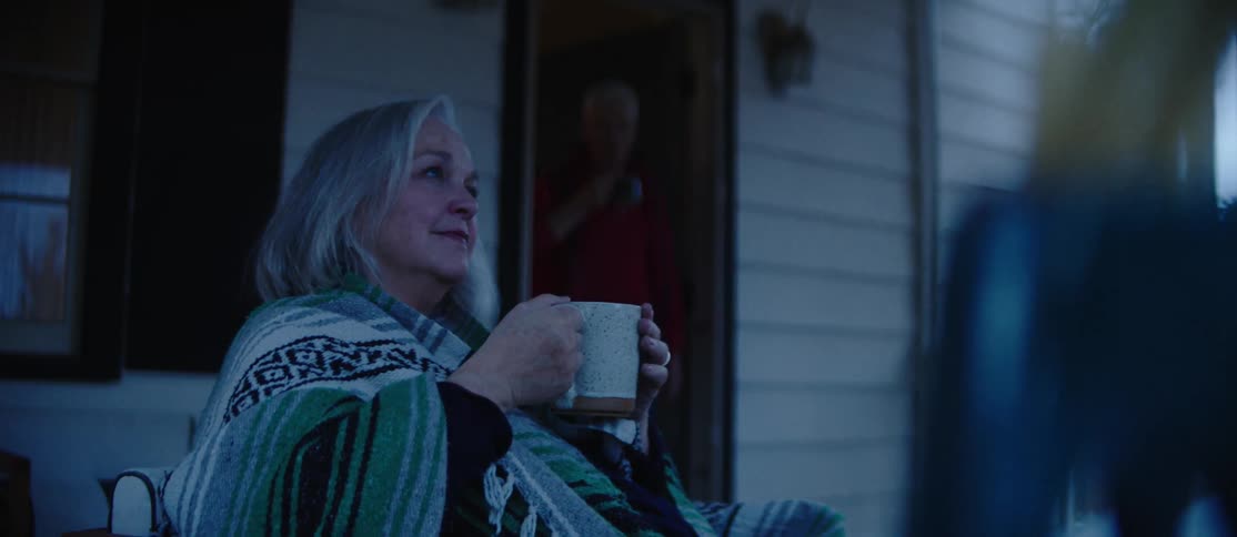 Elderly lady sitting in the backyard of her house drinking from a mug