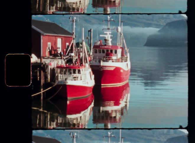 Two red fishing boats are docked at a small harbor nestled beneath a backdrop of mountains