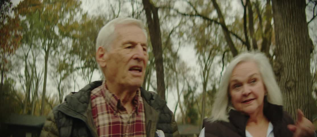 An elderly man and woman chat as they walk through the countryside passing charming cottages